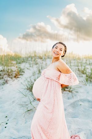 A pink lace dress stands out against white sand dunes and cloudy skies during a beach photoshoot at sunset.