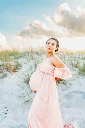 A person in a flowing pink dress twirls joyfully on white sand dunes at sunset.