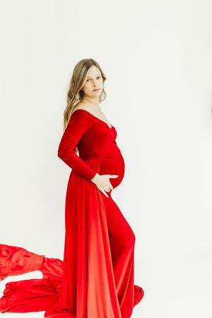 Flowing red maternity gown creates dramatic movement against white studio background.