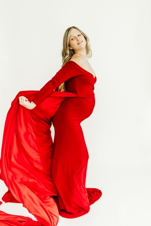 Flowing red velvet maternity gown with dramatic movement against white background.