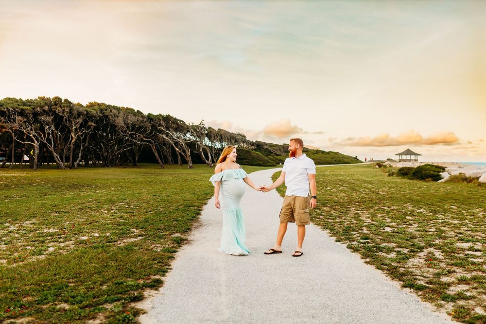 Couple in light blue and white attire walking along a scenic beach path during golden hour.