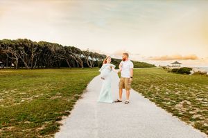A couple walks along a scenic coastal path during golden hour as the sun sets over the beach.
