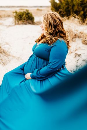A person in a bright blue coat sits on sandy dunes against a light background, shown in a series of similar poses.