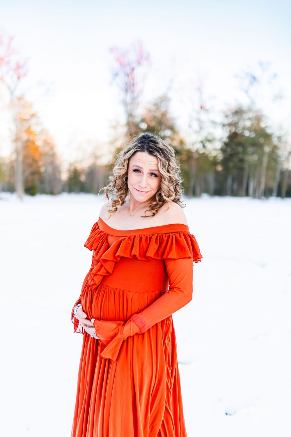 A bright red ruffled maxi dress stands out beautifully against a snowy winter landscape with trees in the background.
