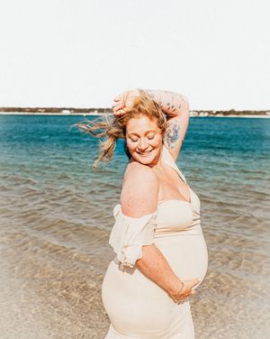 A sequence of photos shows a pregnant woman in a white dress twirling joyfully on a sunny beach with turquoise waters.