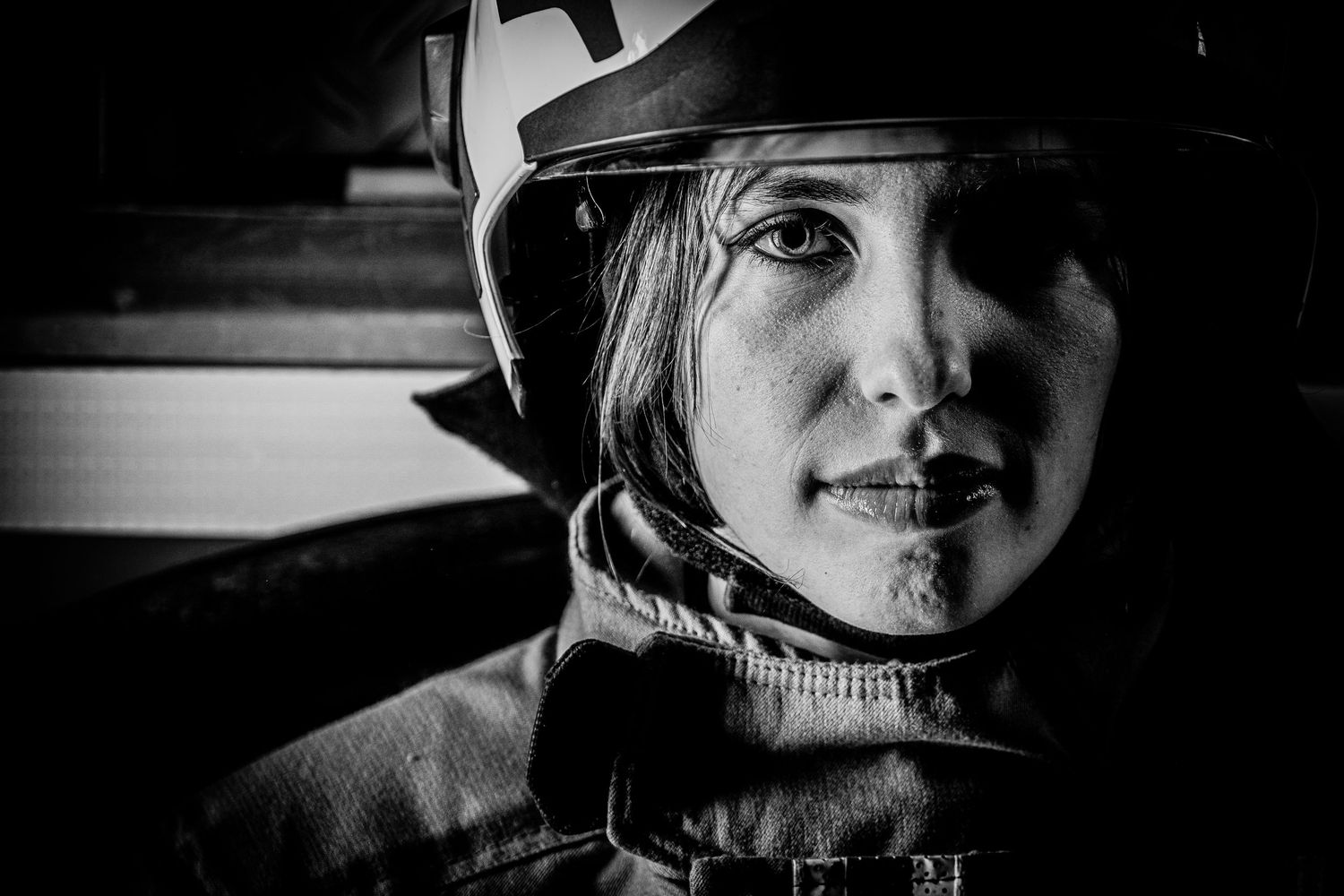 Black and white portrait of a female firefighter wearing a helmet and protective gear.