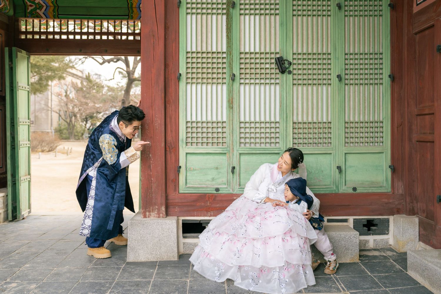 Traditional Korean hanok building with green wooden doors and multiple couples in formal attire posing for photos.