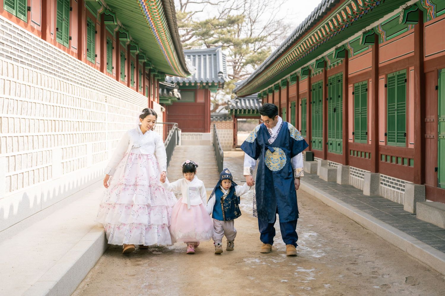 People walk through a traditional Korean palace corridor with green painted wooden beams and white walls.
