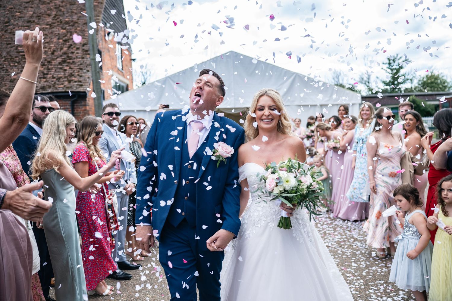 Wedding guests shower newlyweds with white confetti during outdoor celebration in front of mountain backdrop.