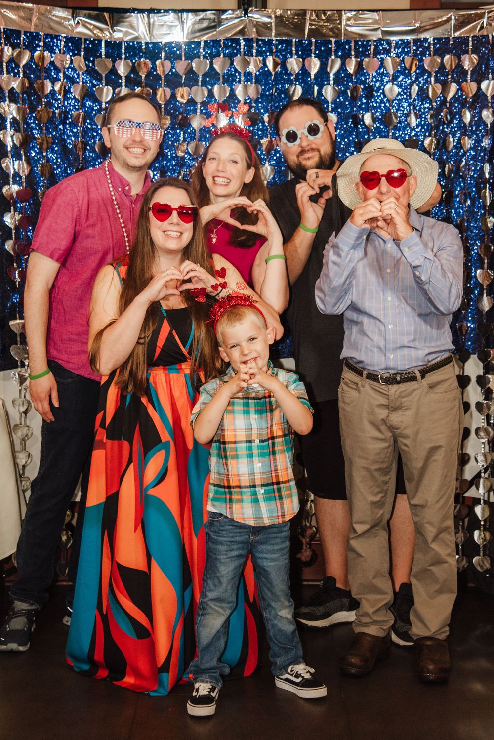 A group poses together against a sparkly blue backdrop at a photo booth party making silly faces and gestures.