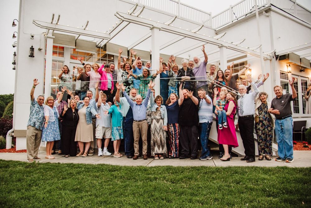 Wedding guests gather under a white tent for a celebratory group photo during an outdoor reception.