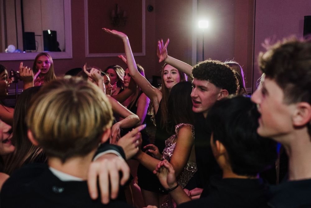 Silhouettes of people dancing and raising their hands at a dimly lit concert or nightclub party.