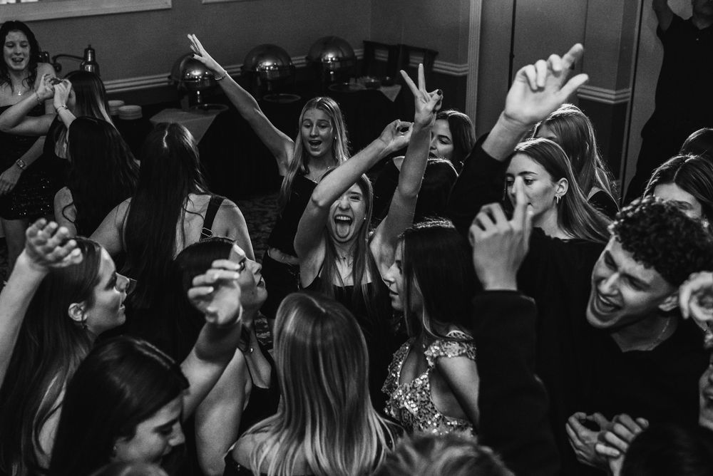 Monochrome shot of an energetic crowd dancing and celebrating at a party with raised hands.