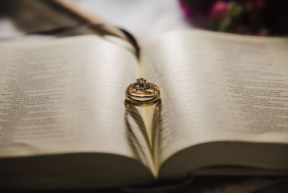 A close-up view of a gold wedding ring resting on an open book with pages fanned out in soft lighting.
