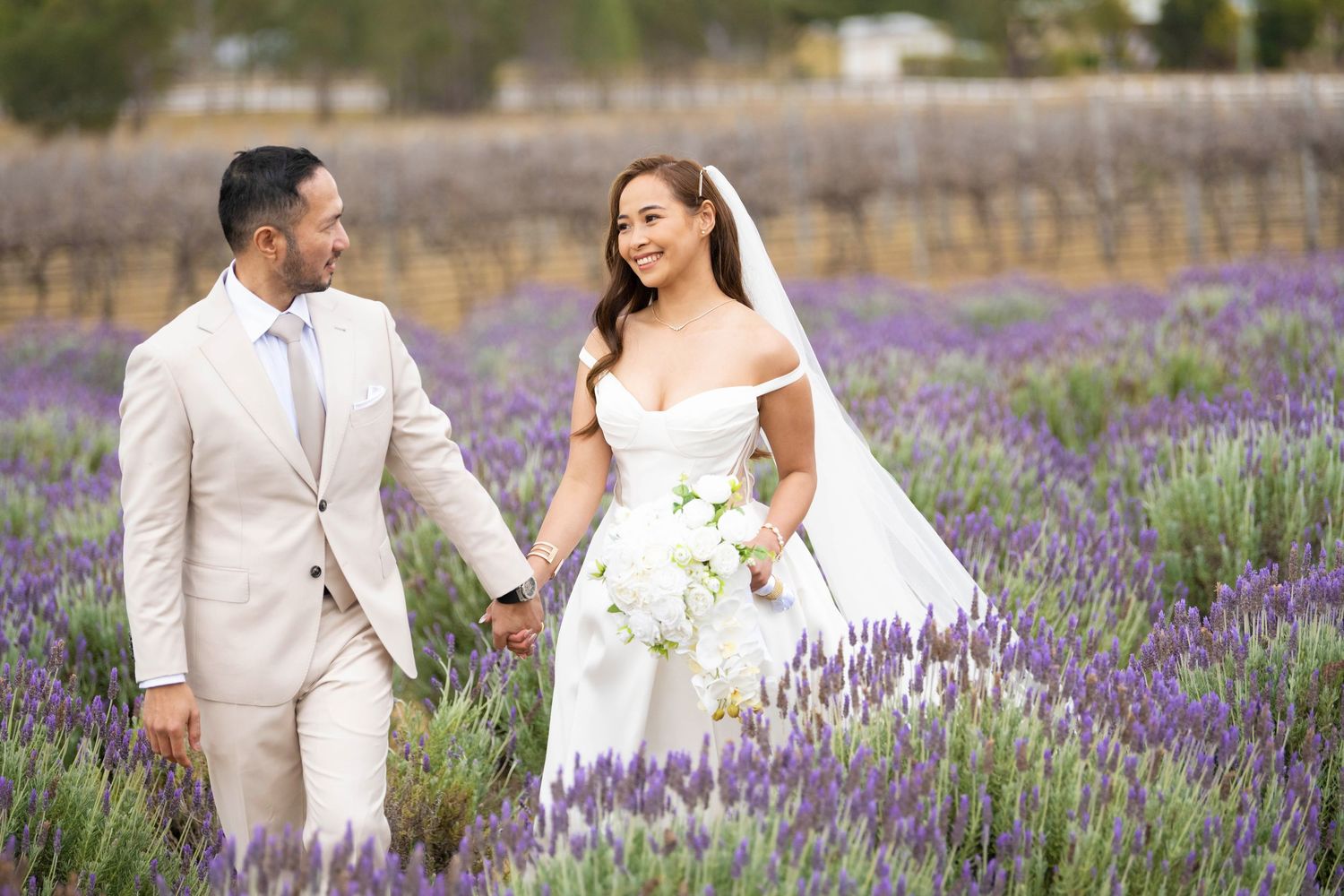 Bride and groom walk hand in hand through a stunning purple lavender field on their wedding day.