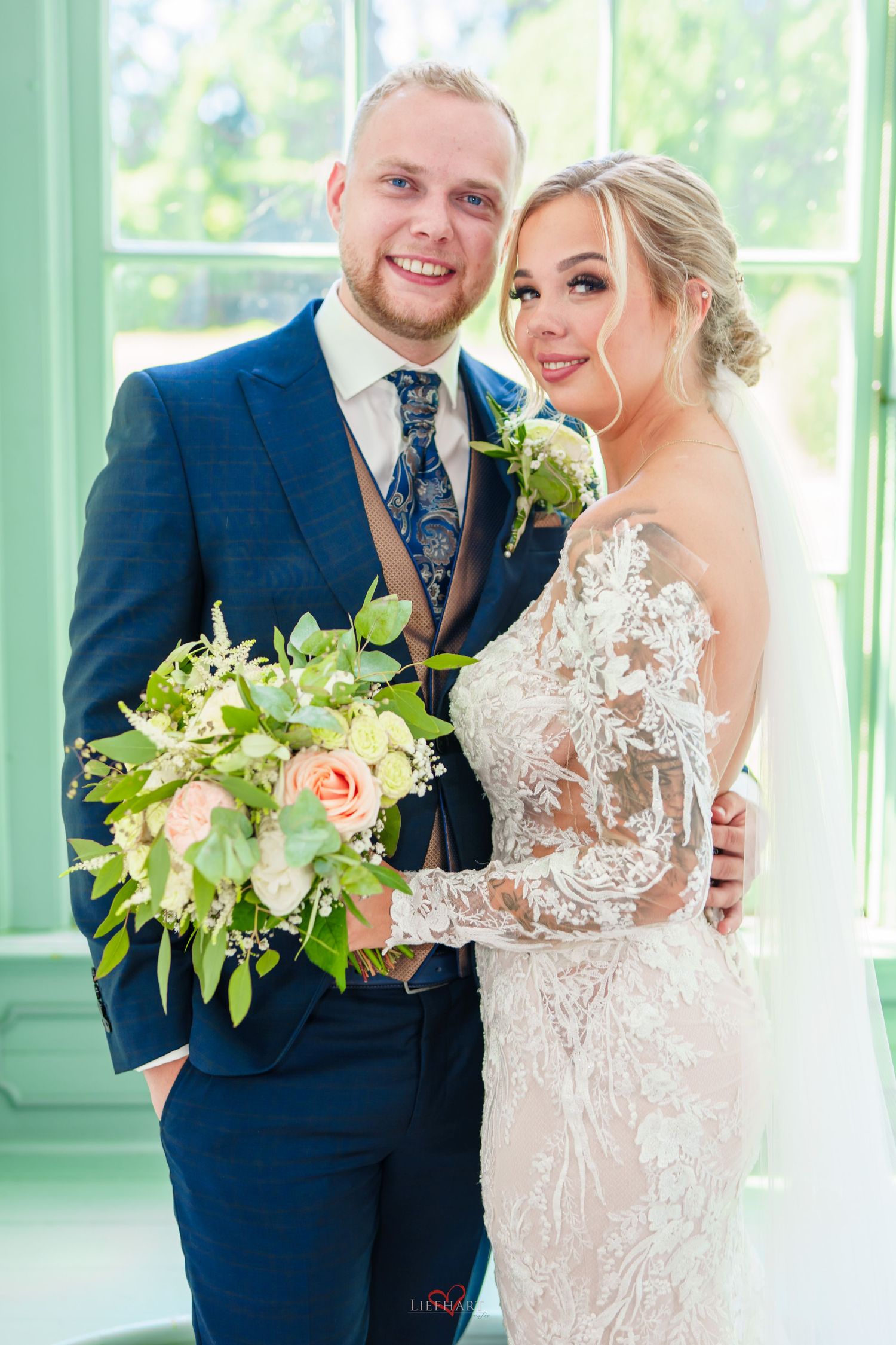 Newlywed couple poses together in formal wedding attire with bride holding peach and white floral bouquet.