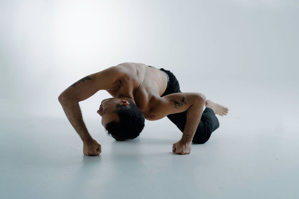 Athletic dancer performs contemporary floor movement in dramatic backbend pose against light background.
