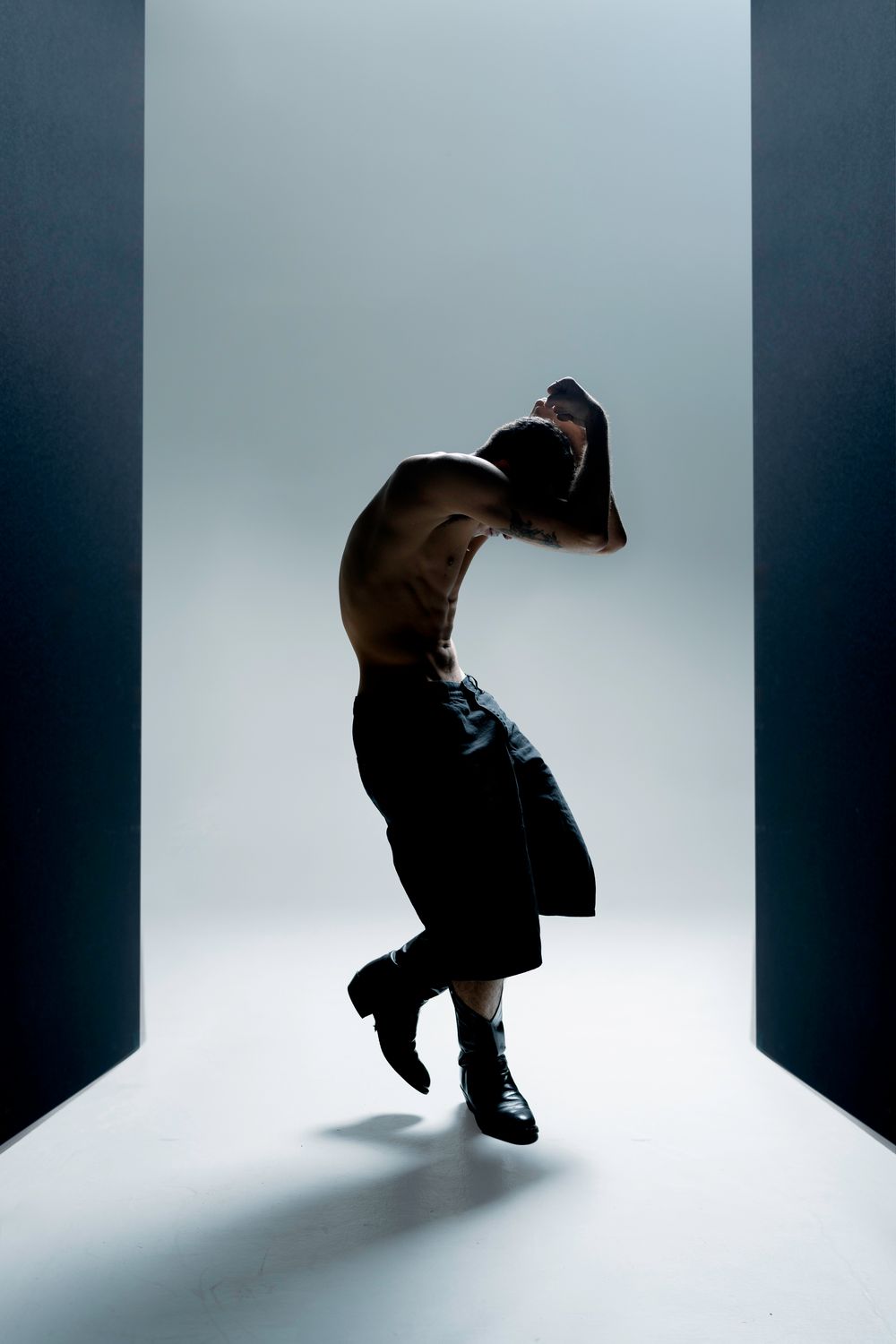 Silhouetted figure performs dynamic dance movements in a minimalist white space with dramatic lighting and shadows.