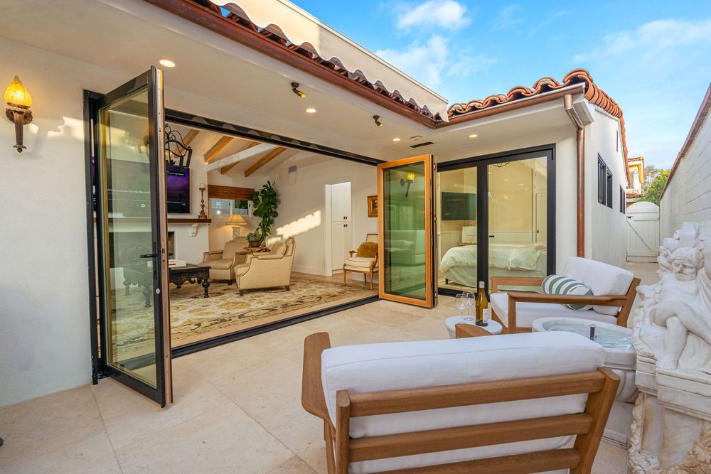 Luxury patio with folding glass doors opening to a modern living room with beige furniture and Mediterranean style architecture.