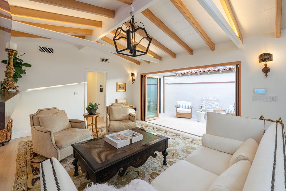 A bright modern living room with exposed wooden beams, white furniture, and large windows overlooking a scenic view.