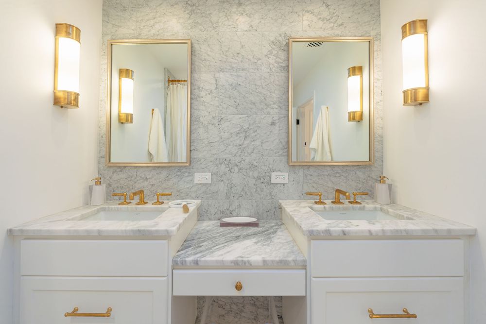 Modern bathroom interior with marble walls, gold sconces, and white vanity showcasing elegant transitional design details.