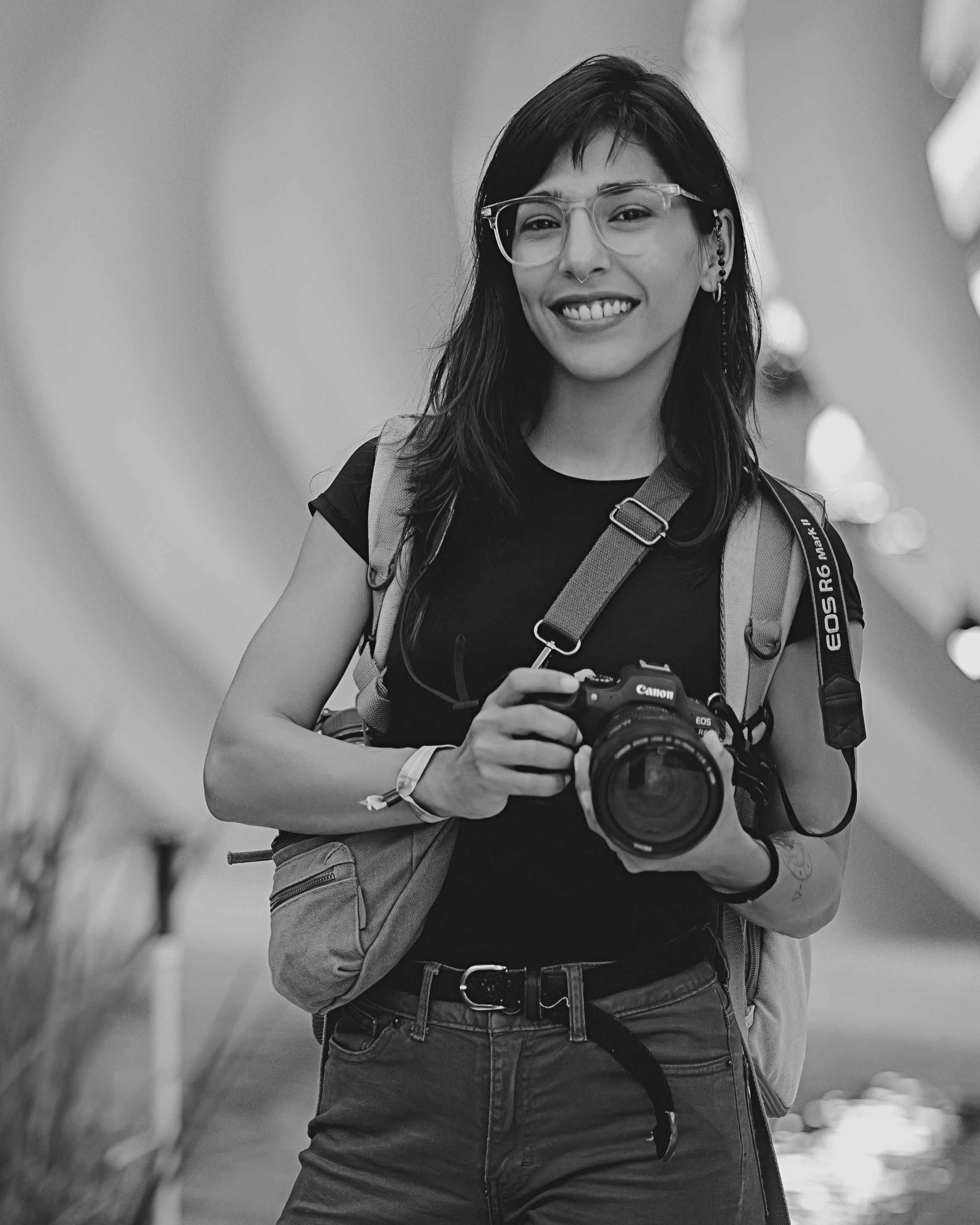 A photographer wearing dark clothing and glasses practices different poses while holding a camera.