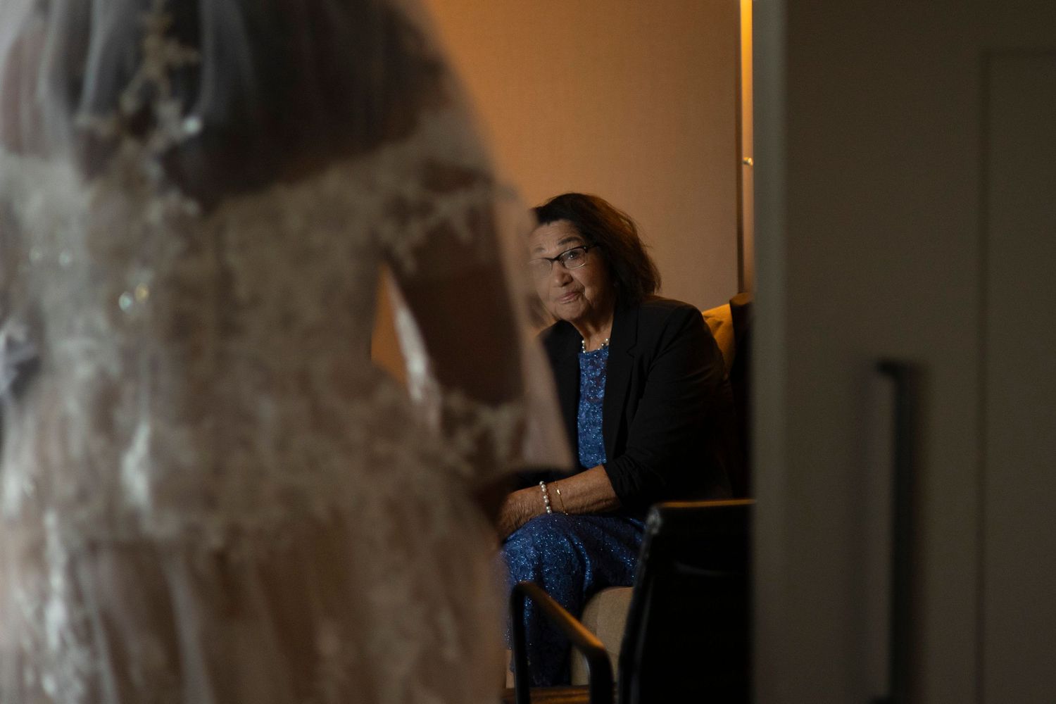 A person in a dark room stands in front of a window with dramatic lighting and shadows creating a moody atmosphere.
