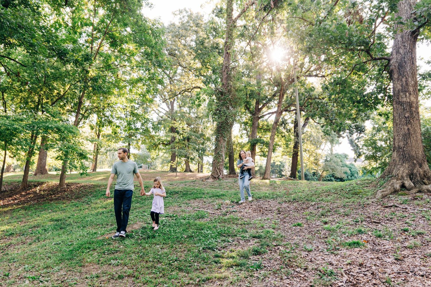 People walking along a wooded path in a park on a sunny afternoon with sunlight filtering through the trees in Charlotte NC.