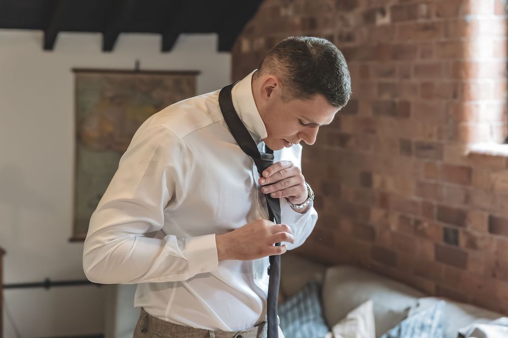 Documentary style wedding photo of groom putting on his tie.