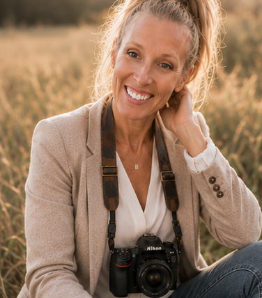 A self portrait of a woman smiling with a camera handing around her neck in a field