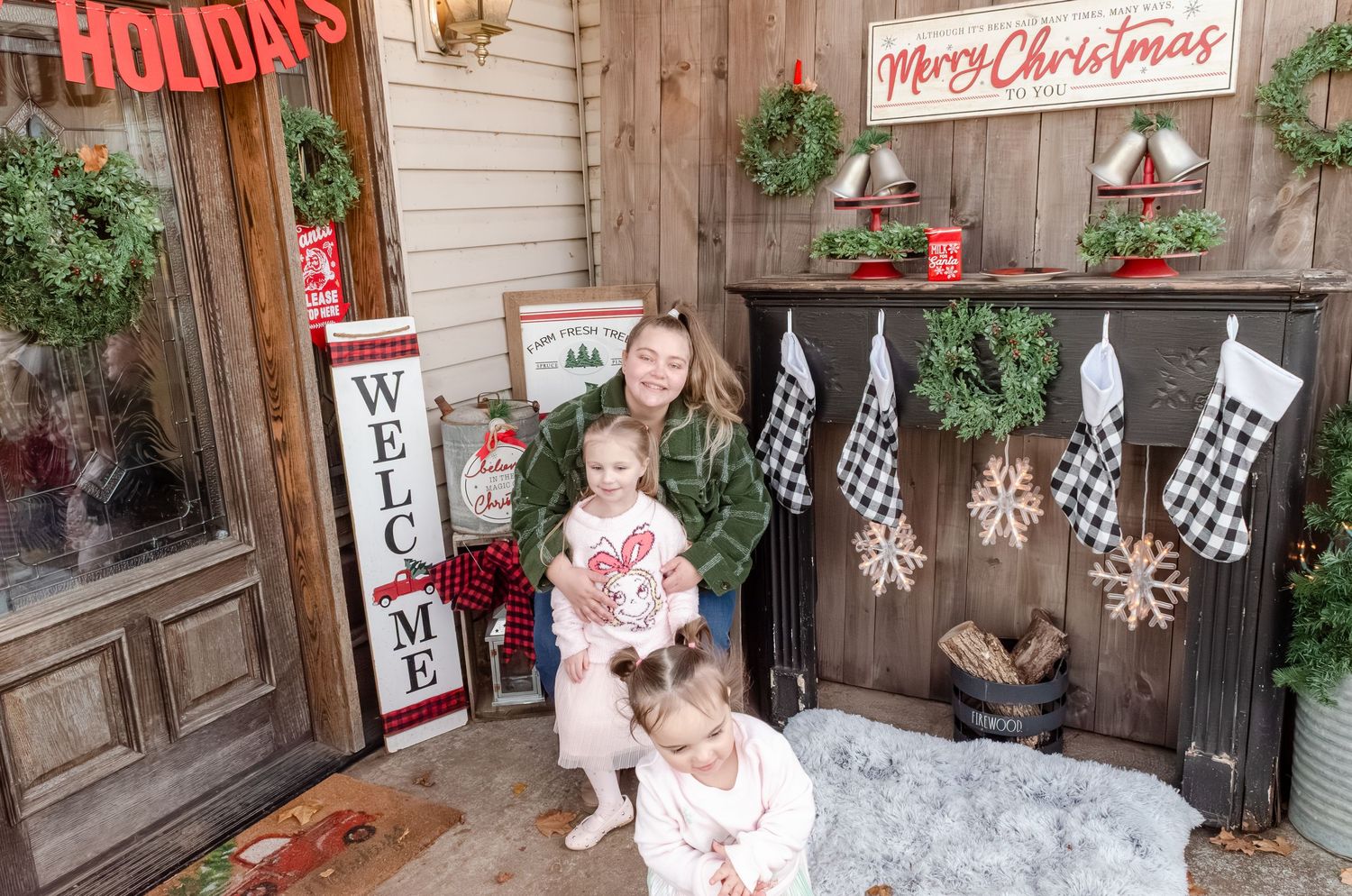 Festive Christmas porch display with wreaths, stockings, and rustic holiday decor against white siding and wood panels.