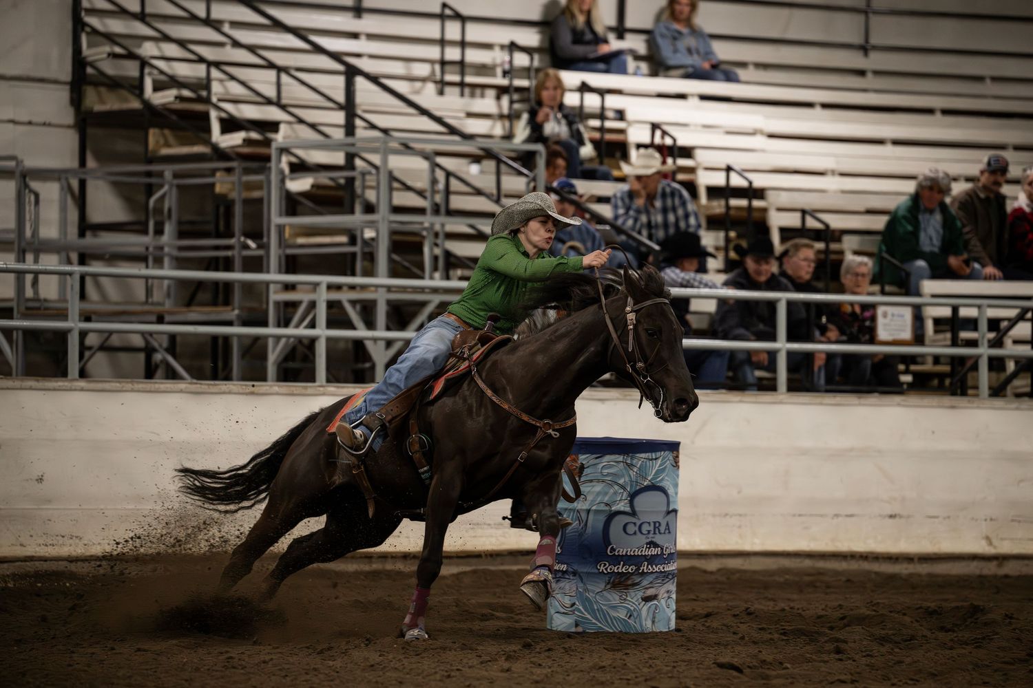 Barrel racing competitor guides horse around blue barrel during rodeo competition in indoor arena.