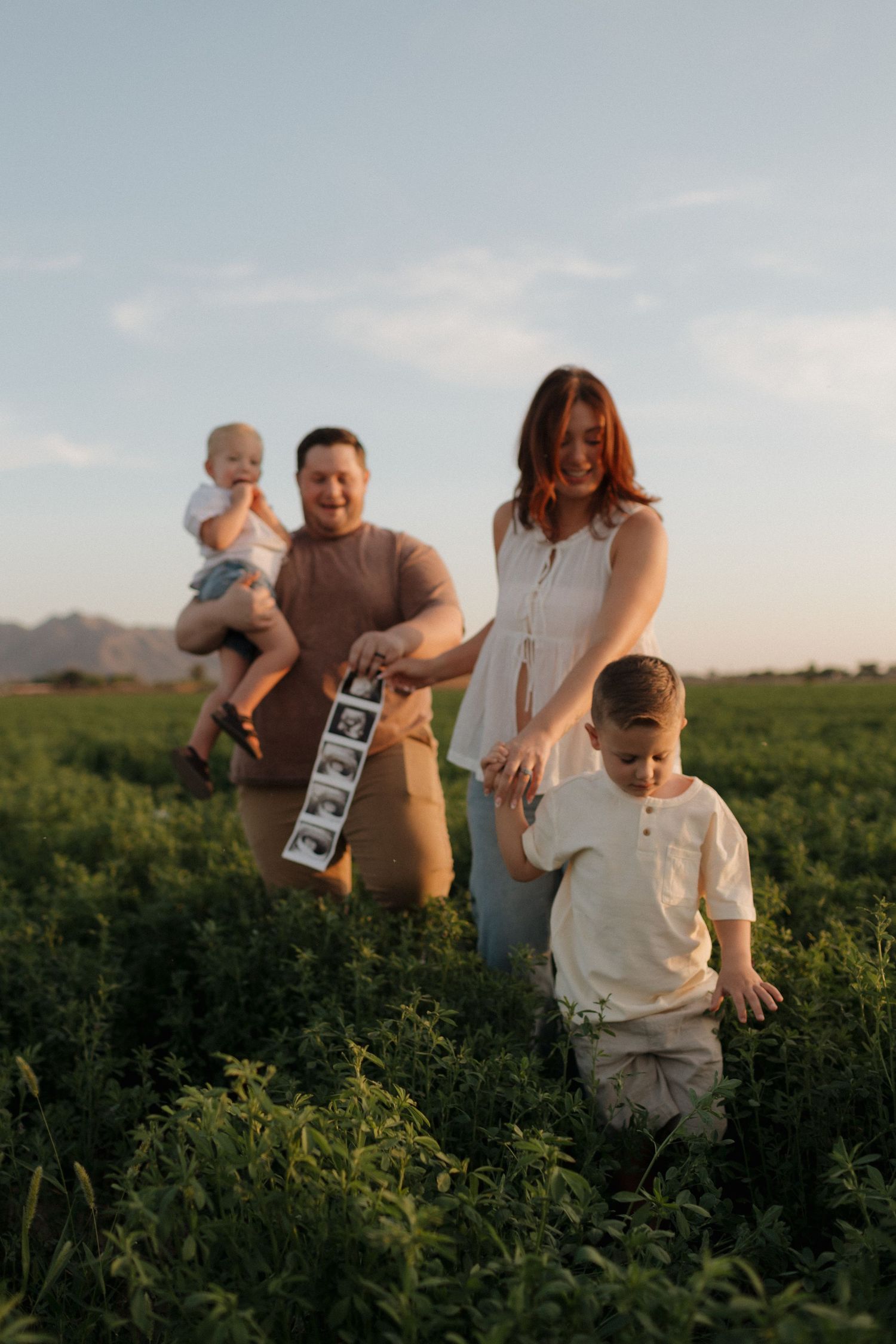 Outdoor maternity announcement photo with couple holding ultrasound prints in desert setting.