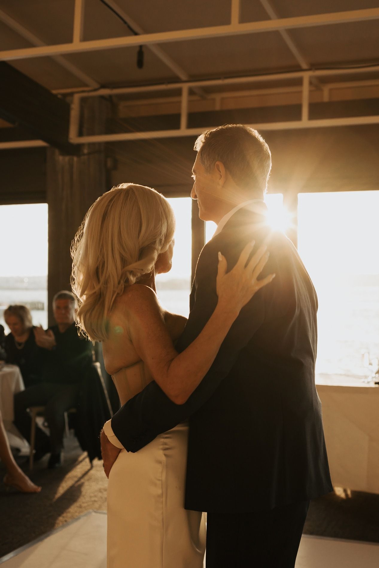 A romantic couple dancing together in silhouette against warm sunlight streaming through windows in an indoor venue.