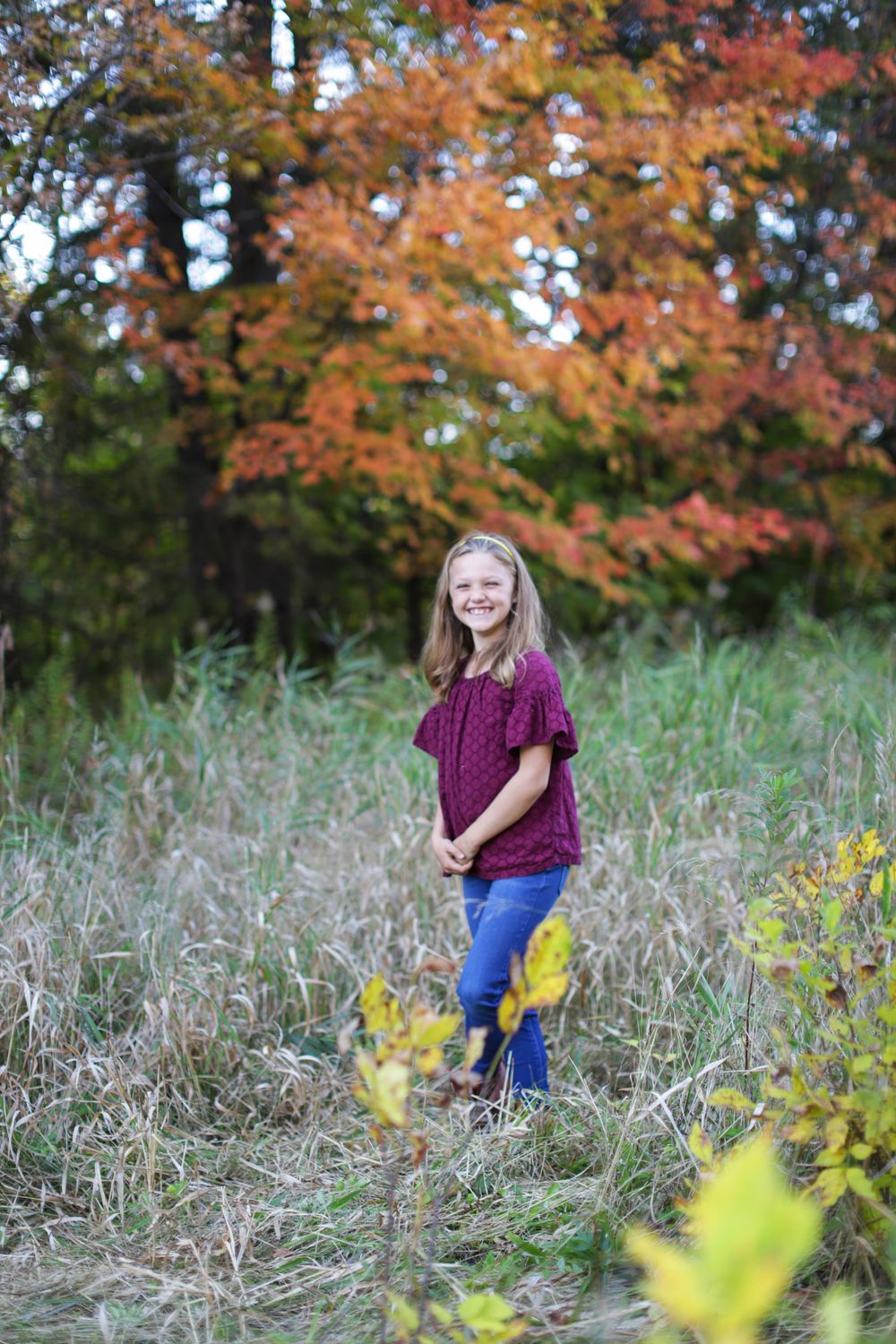 Fall foliage creates a colorful backdrop in a field with tall grass and yellow wildflowers.
