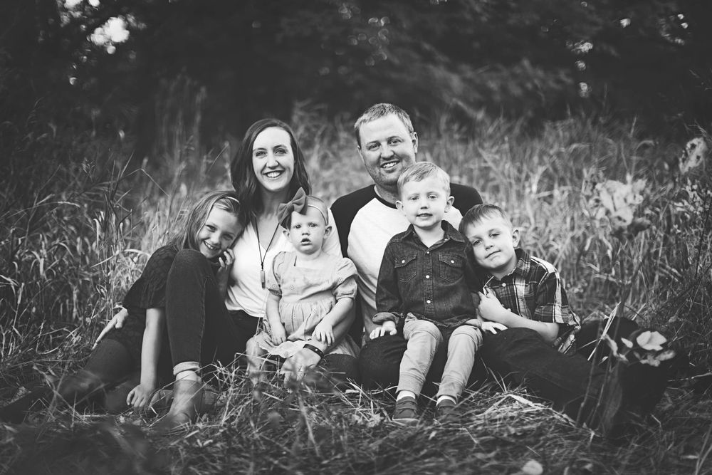 A group of people lying in tall grass outdoors enjoying a casual summer photoshoot together.
