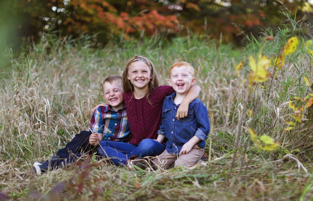 A playful outdoor autumn photoshoot in tall grass with yellow wildflowers and natural lighting.