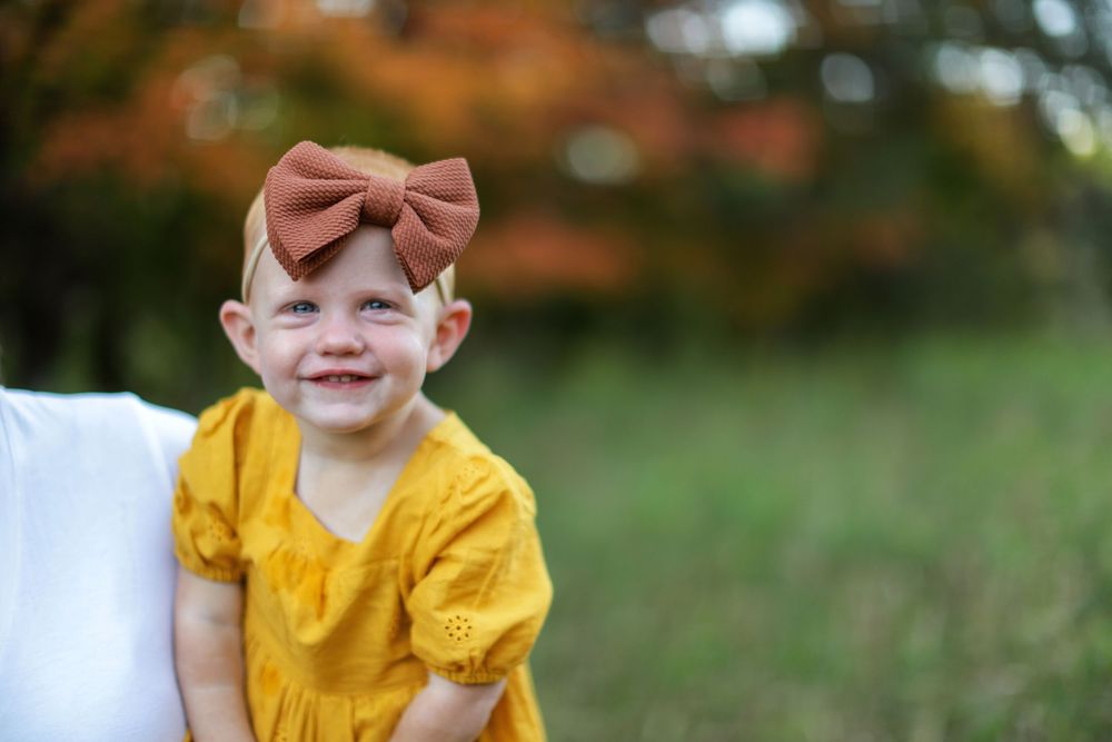 A young person wearing a yellow ruffled top smiles while posing outdoors in a natural setting.
