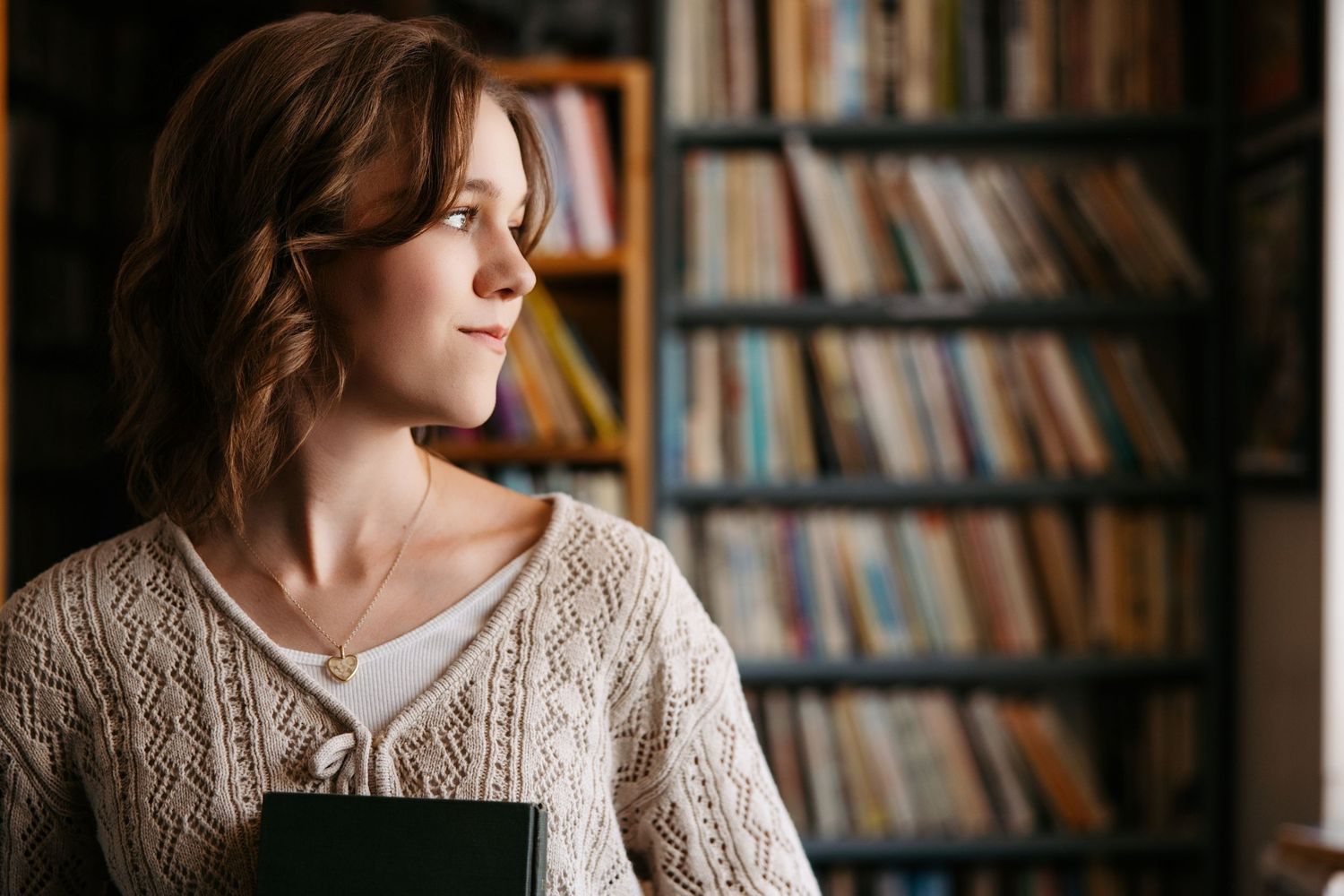 A person in a cozy sweater and jeans browses books in a narrow aisle of a charming bookstore.