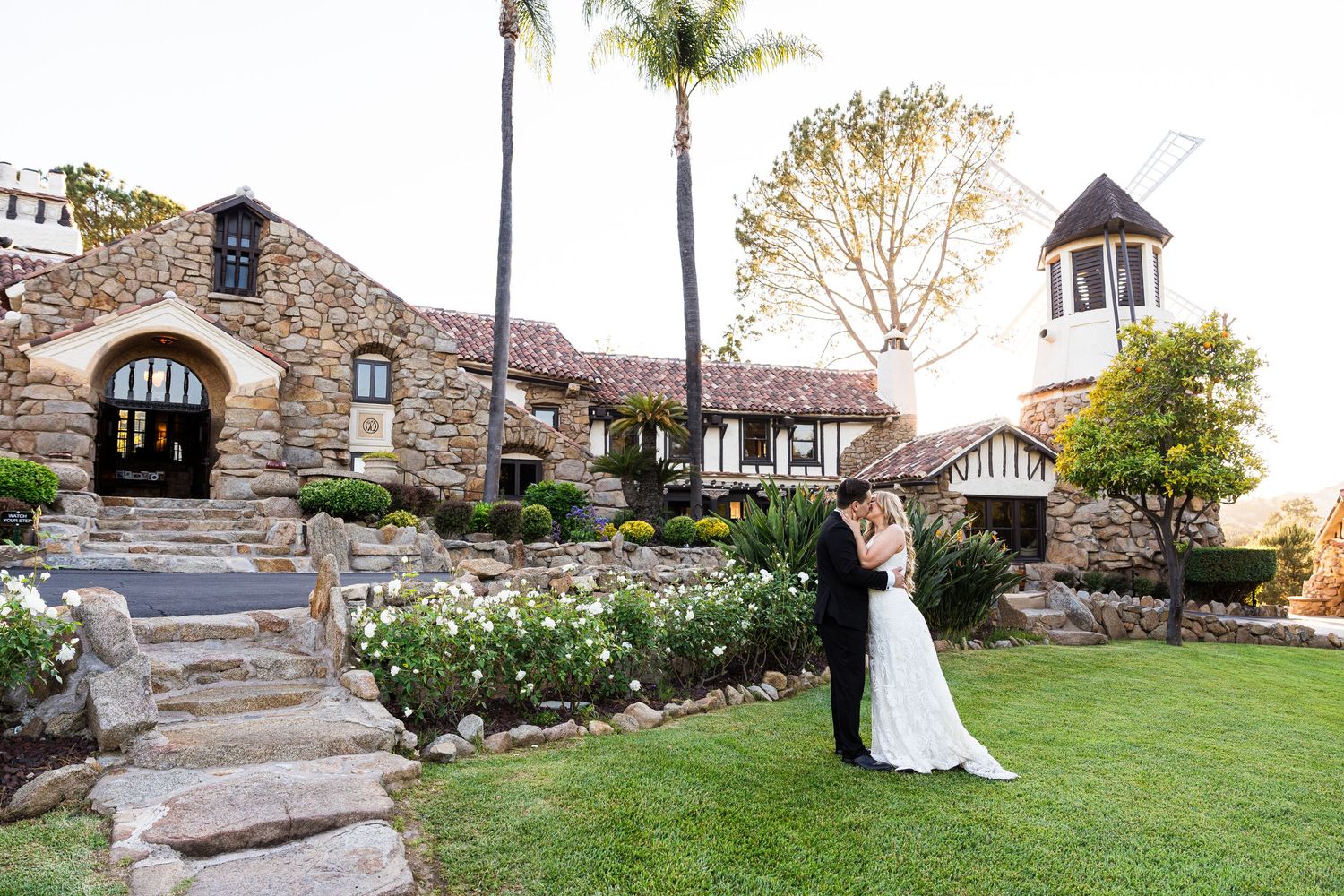 A romantic couple embraces near a rustic stone wall during their wedding photo session at a historic venue.