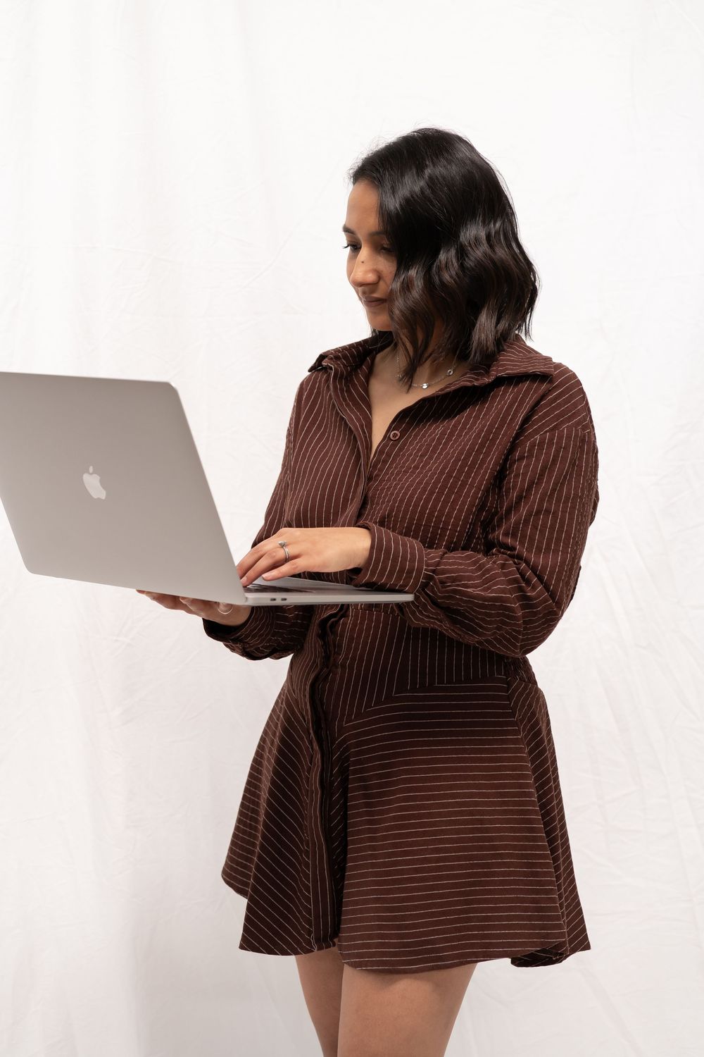 Person in brown striped dress working on MacBook laptop against white background.
