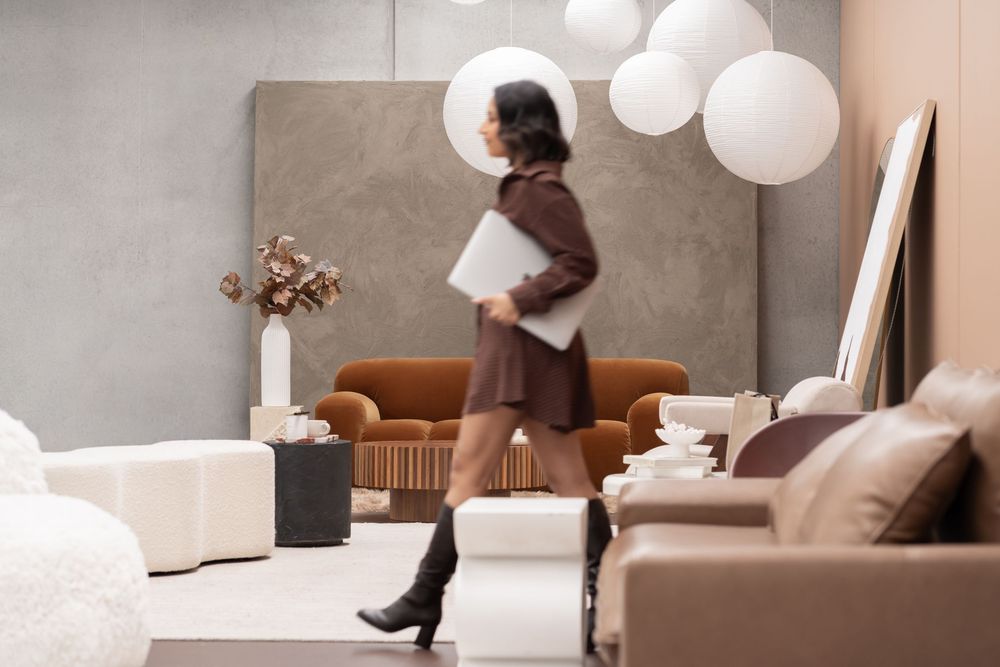 Person in black socks sits on a modern beige couch in a minimalist living room with white walls and pendant lights.