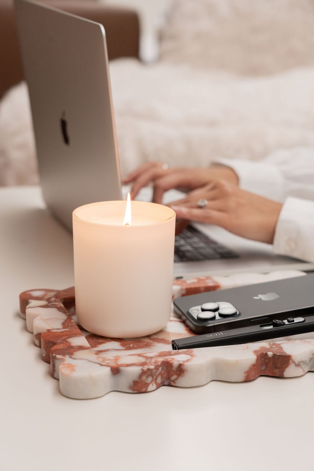 Cozy workspace scene featuring a lit candle, laptop, and marble-patterned decorative elements on a soft surface.