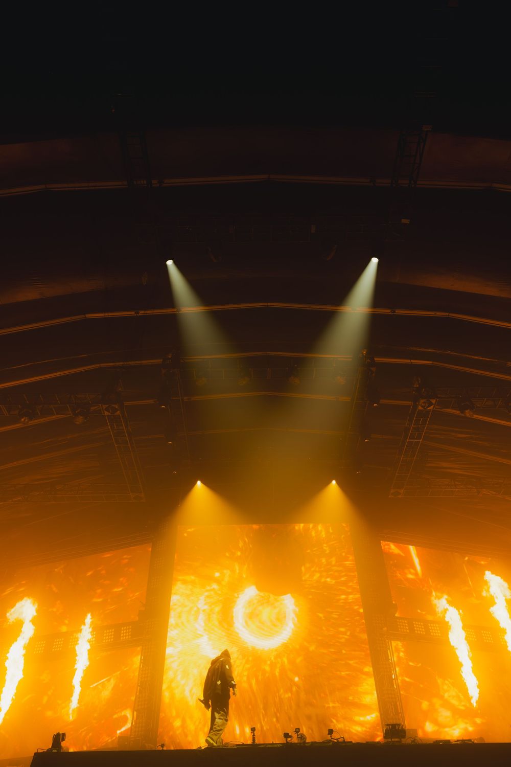 Dramatic concert stage lighting creates a golden glow with multiple spotlights illuminating a dark performance space.