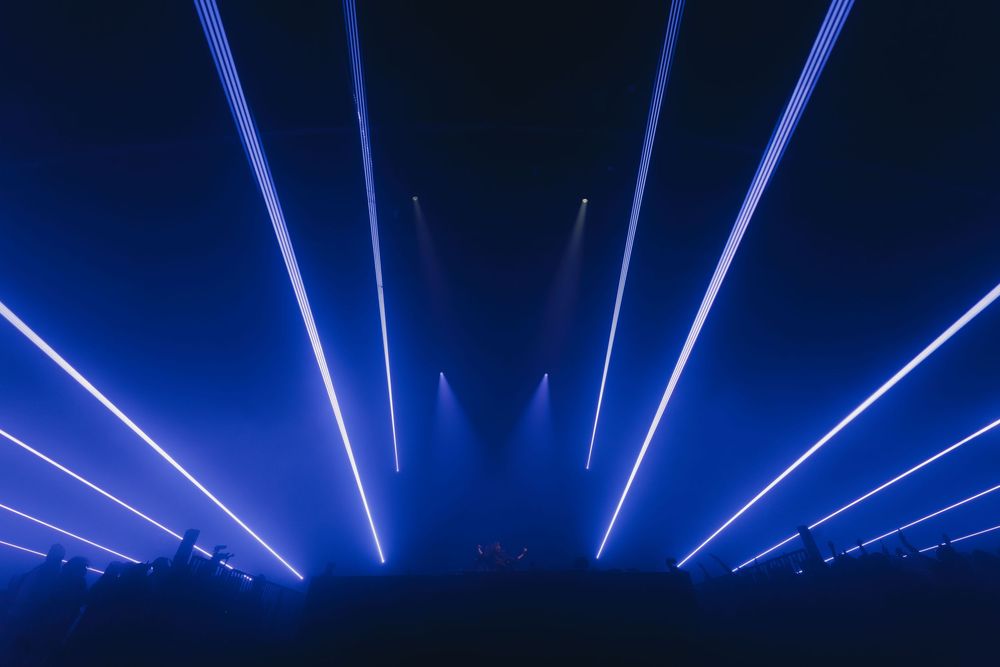 Blue laser beams shine upward in a symmetrical pattern against a dark background at an entertainment venue.