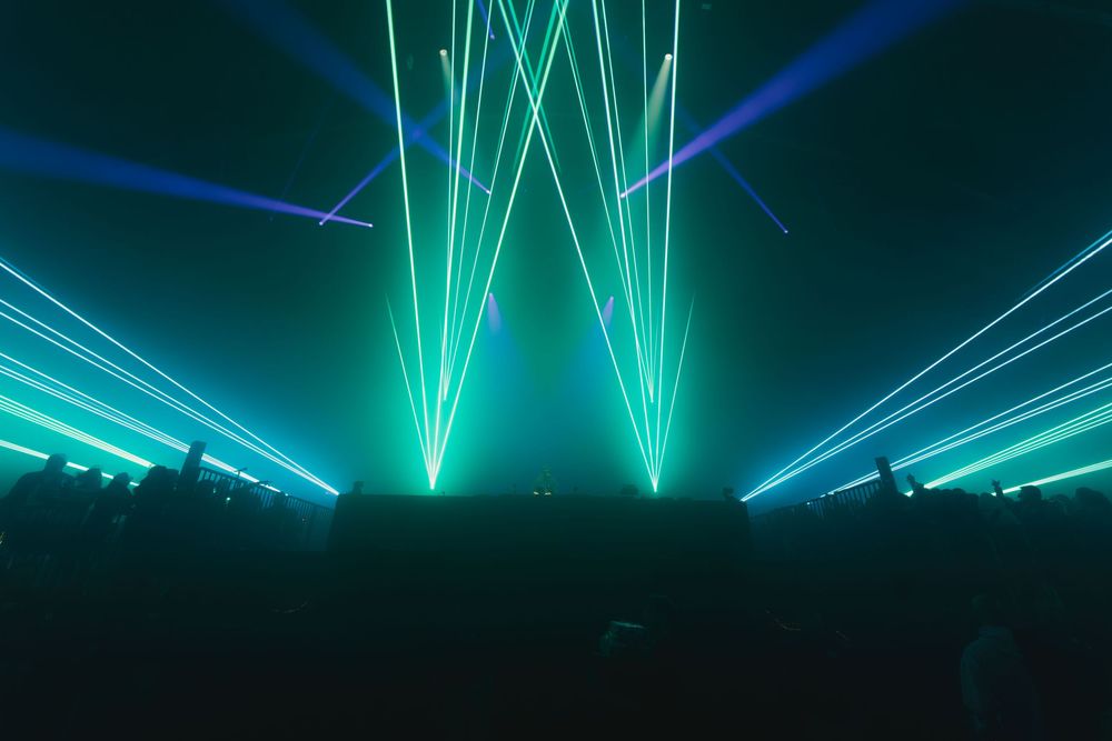 Vibrant turquoise and blue laser beams illuminate a dark concert venue creating dramatic lighting effects.