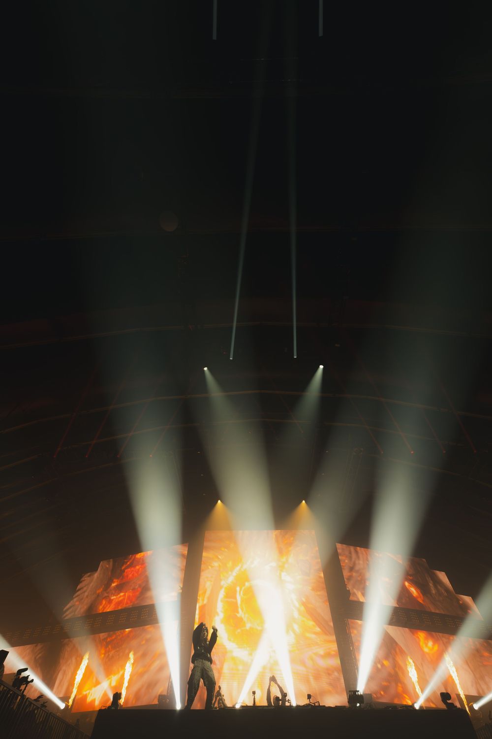 Dramatic concert stage lighting with orange flames and white spotlights illuminating a dark performance space.