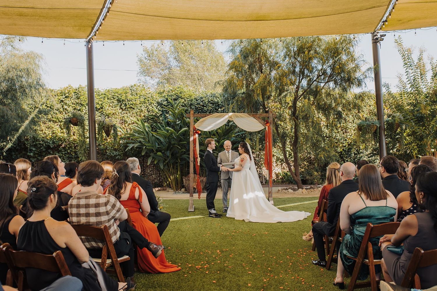 Outdoor wedding ceremony guests seated in rows of white chairs on a lawn during golden hour sunlight at River Garden Weddings and Events..
