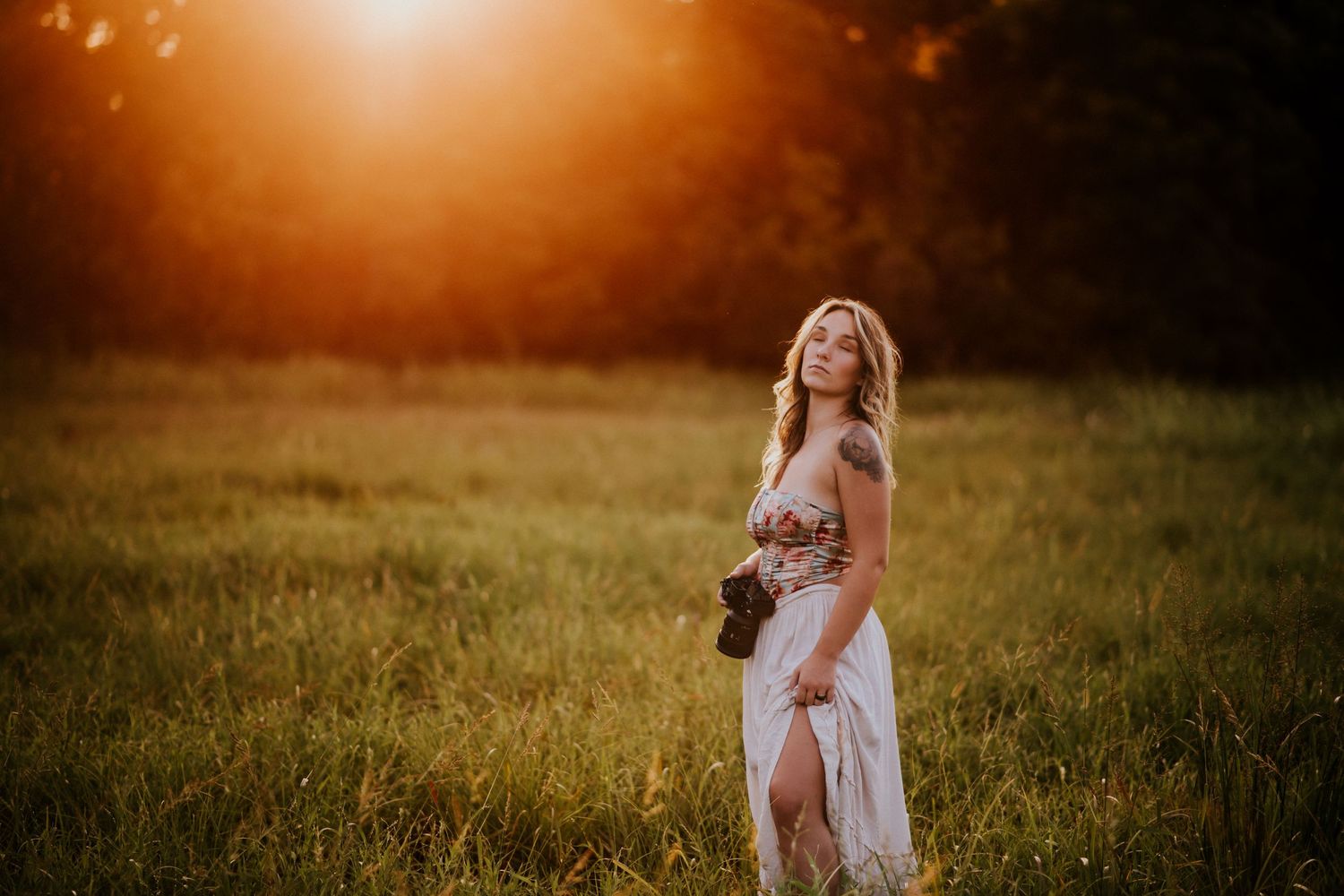 Branding photo of a photographer in a field as the sunsets behind the trees with her camera in her hand in Clarksville, Tennessee.