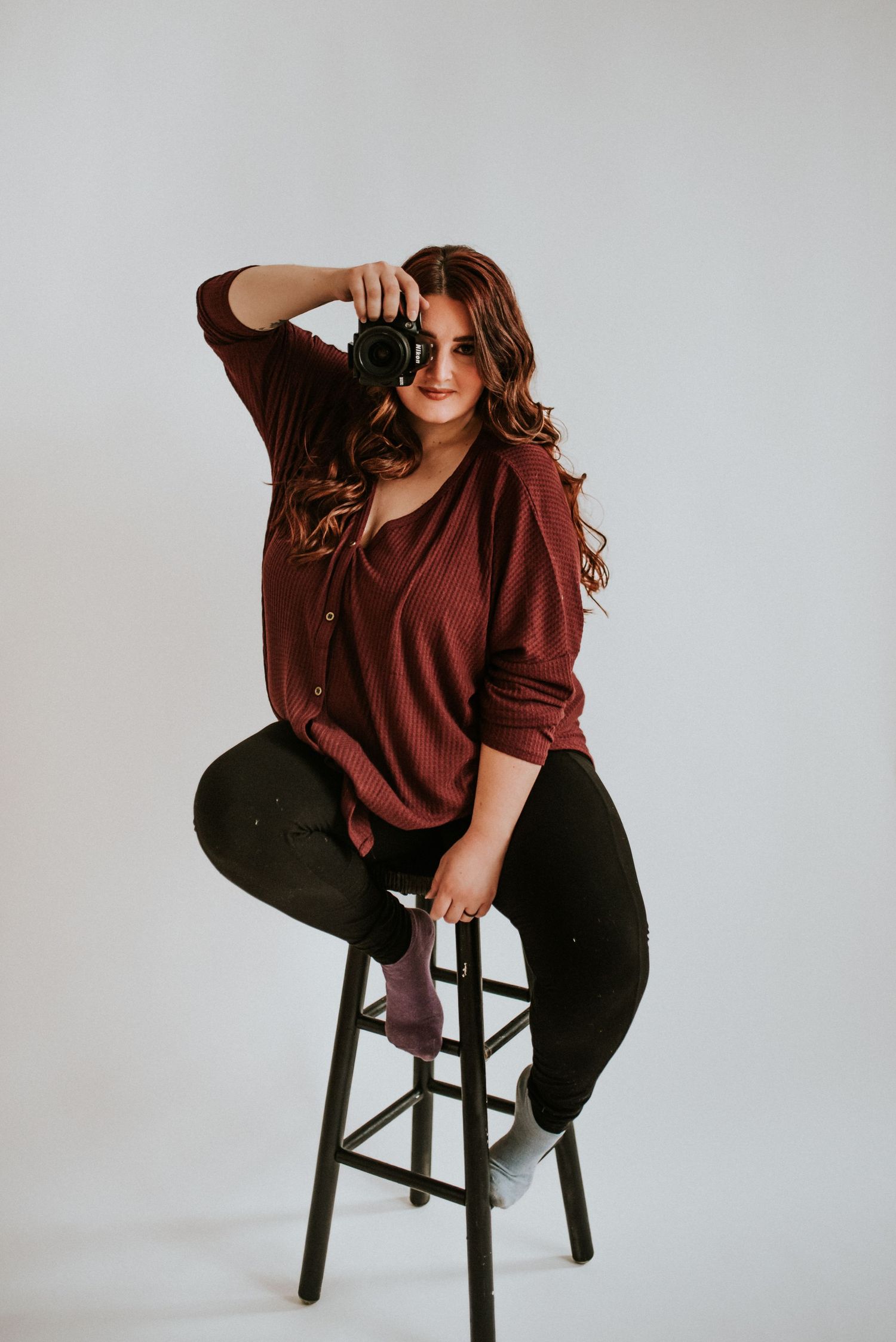 Branding photo of a photographer sitting on a stool in a studio in Clarksville, Tennessee with the camera to her face.